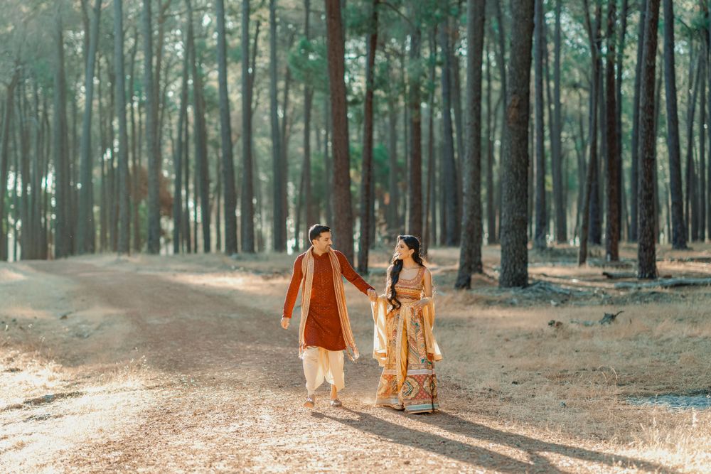 Couple in traditional Indian attire walking hand in hand down a forest path.