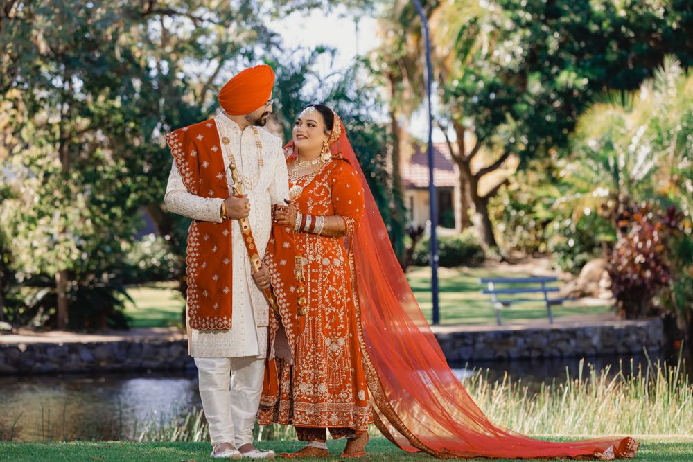 Couple in traditional Indian wedding attire pose together in garden setting.