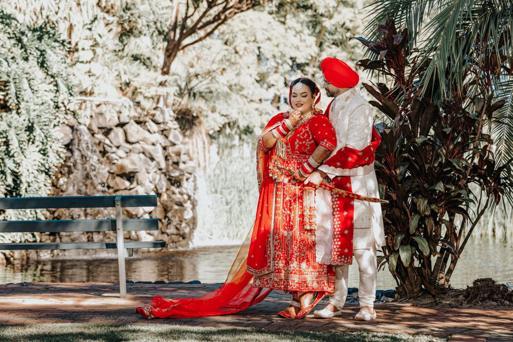Newlywed couple in red and white Indian wedding attire pose together in tropical garden.