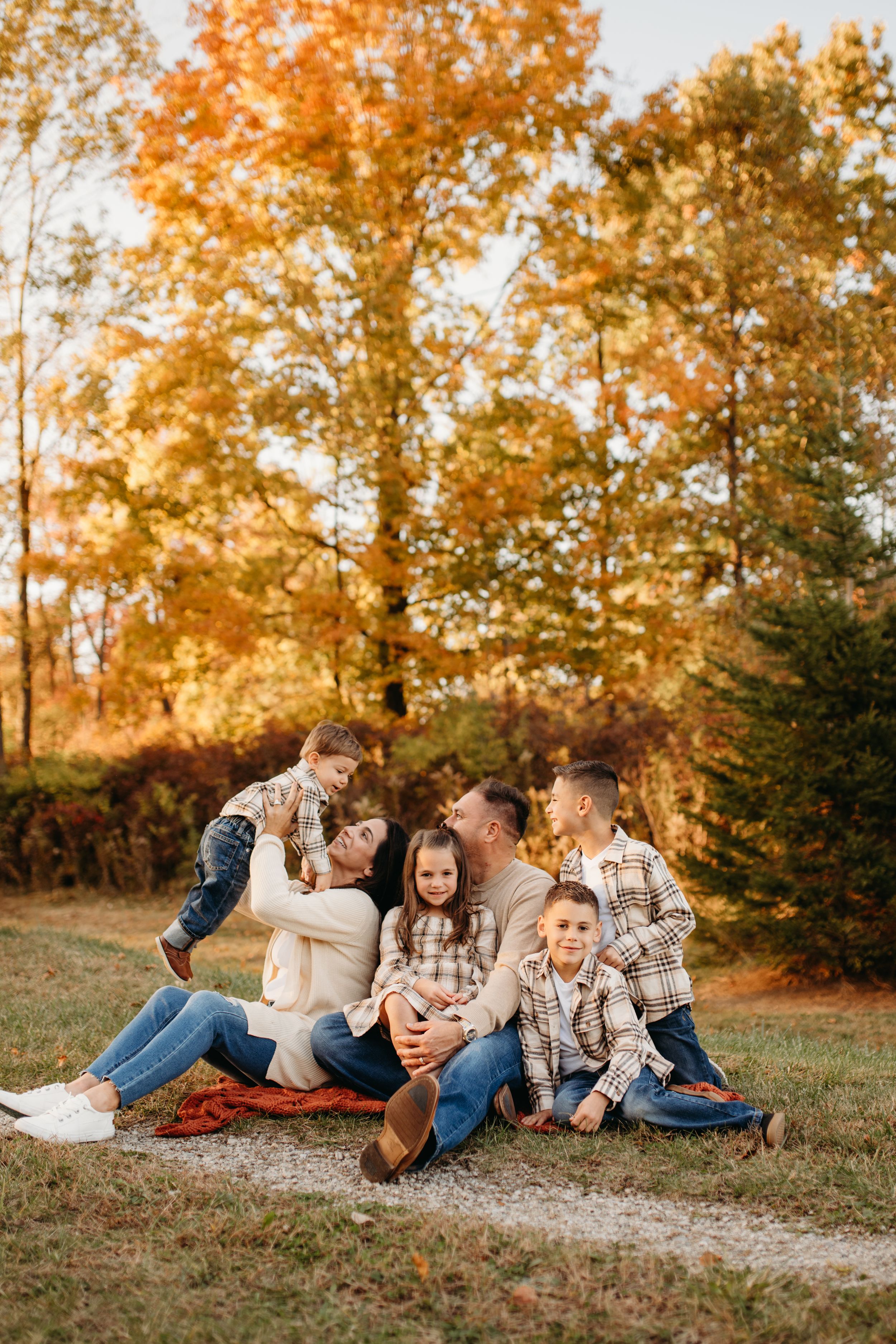 Family sitting together on a blanket during sunset with fall foliage in the background.