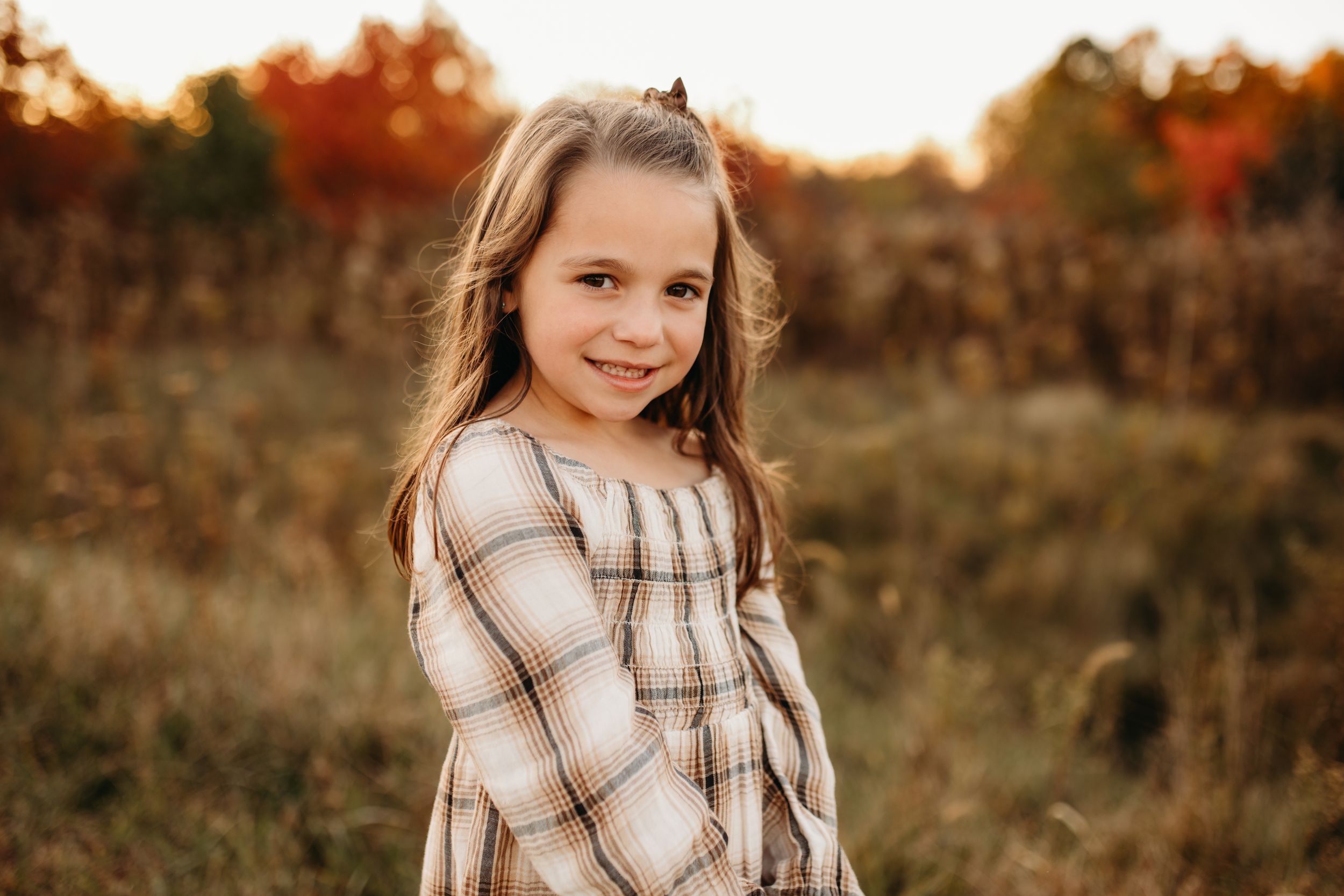 A person in plaid shirt poses in a golden autumn field at sunset.