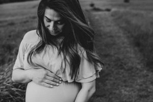 Black and white portrait of expectant mother cradling baby bump outdoors.