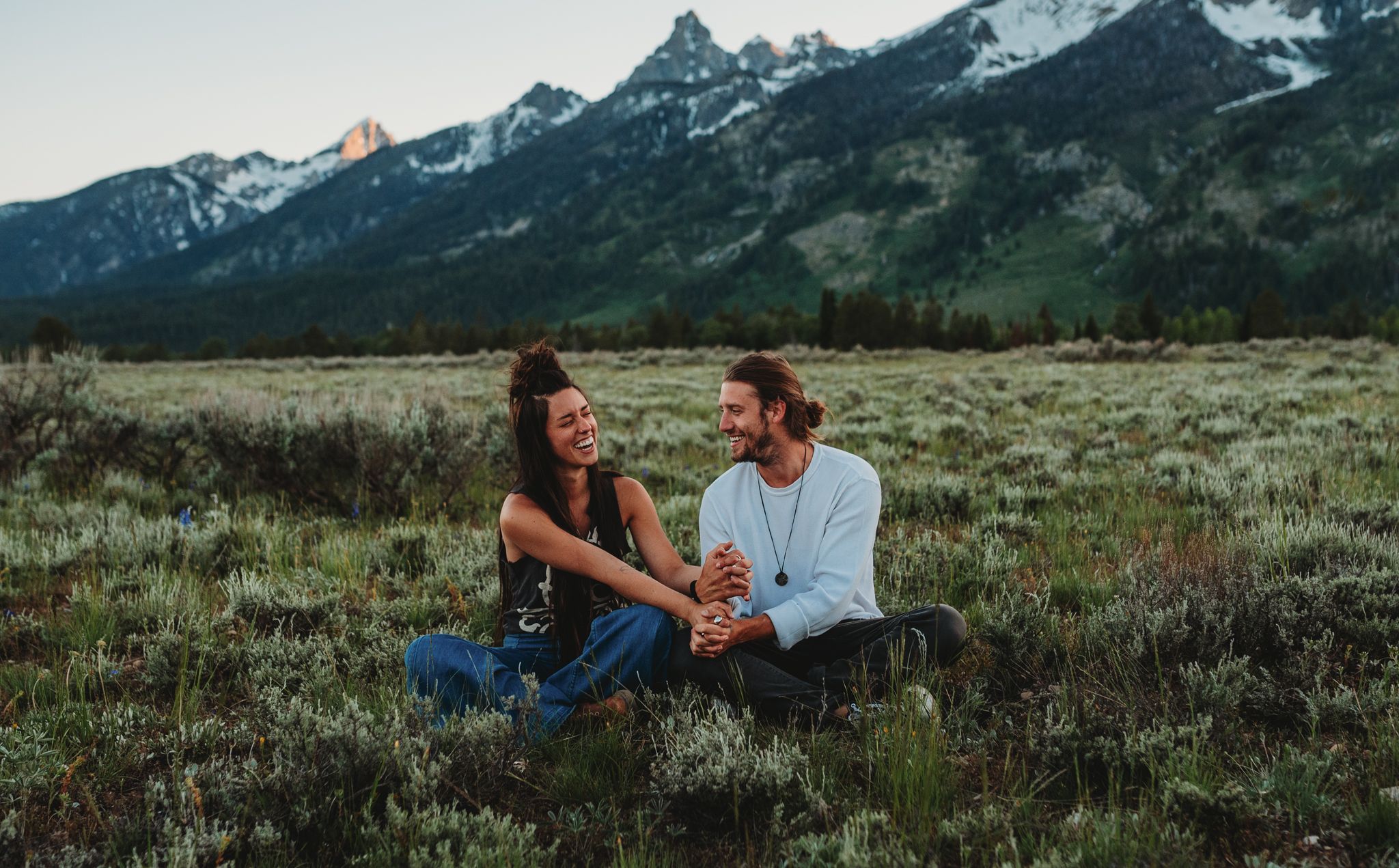 Couple enjoying sunset moment together in mountain meadow with snow-capped peaks in background.