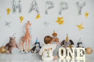 First birthday party decoration setup with silver HAPPY balloon letters, stuffed animals and gold star decorations.