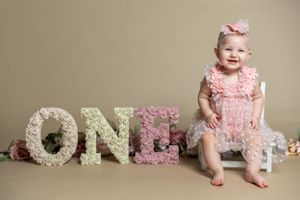 First birthday portrait setup with floral decorated ONE letters against beige background.