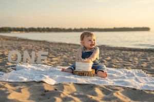Baby having a cake smash photo session on a beach blanket at sunset.