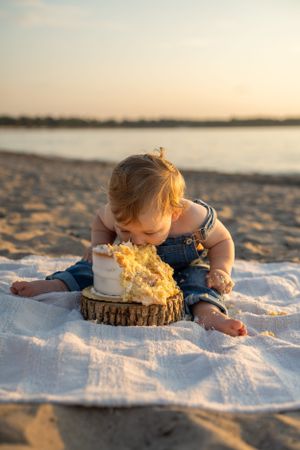 Baby reaching towards a smashed cake on a wooden slice during golden hour at the beach.