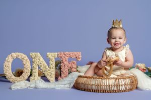 A series of milestone photos showing a baby's first year growth with glittery gold 'ONE' letter decorations.