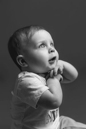 A black and white photo series shows a baby looking upward in different poses while wearing a light-colored shirt.