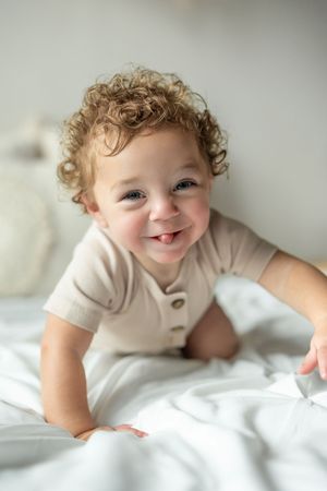 A series of photos showing a happy toddler with curly hair lying on white bedding.
