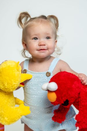 Toddler in blue overalls holds stuffed Sesame Street characters.