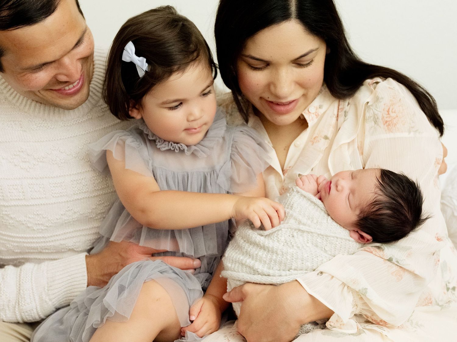 Intimate portrait of figure in white shirt holding newborn baby against bright background.