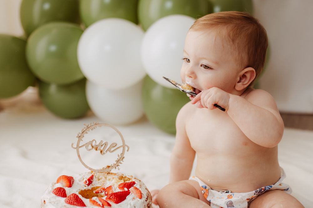Baby's first birthday cake smash photo session with green and white balloons.