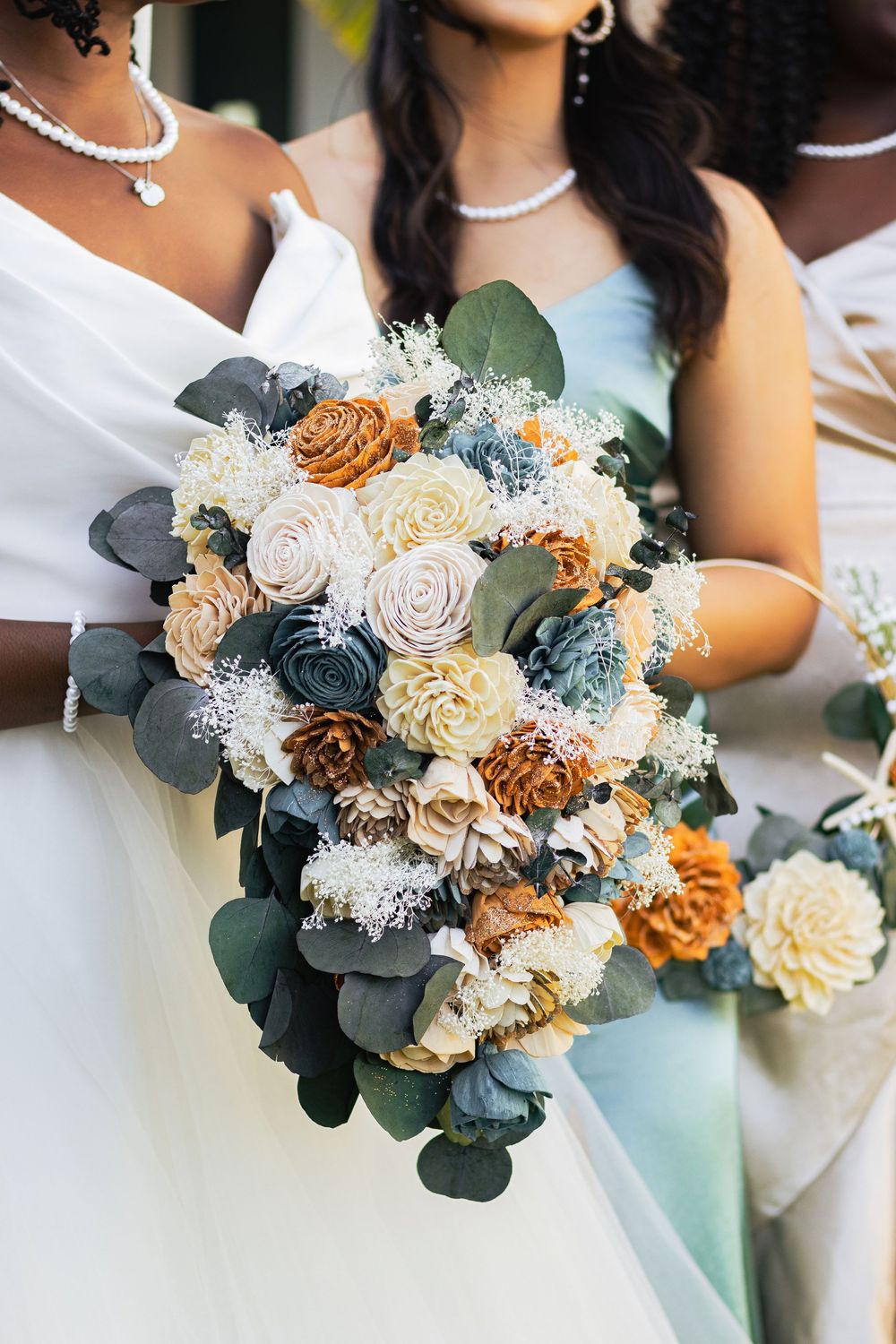 Wedding bouquet featuring cream and rust sola wood flowers with blue eucalyptus and baby's breath details arranged elegantly.