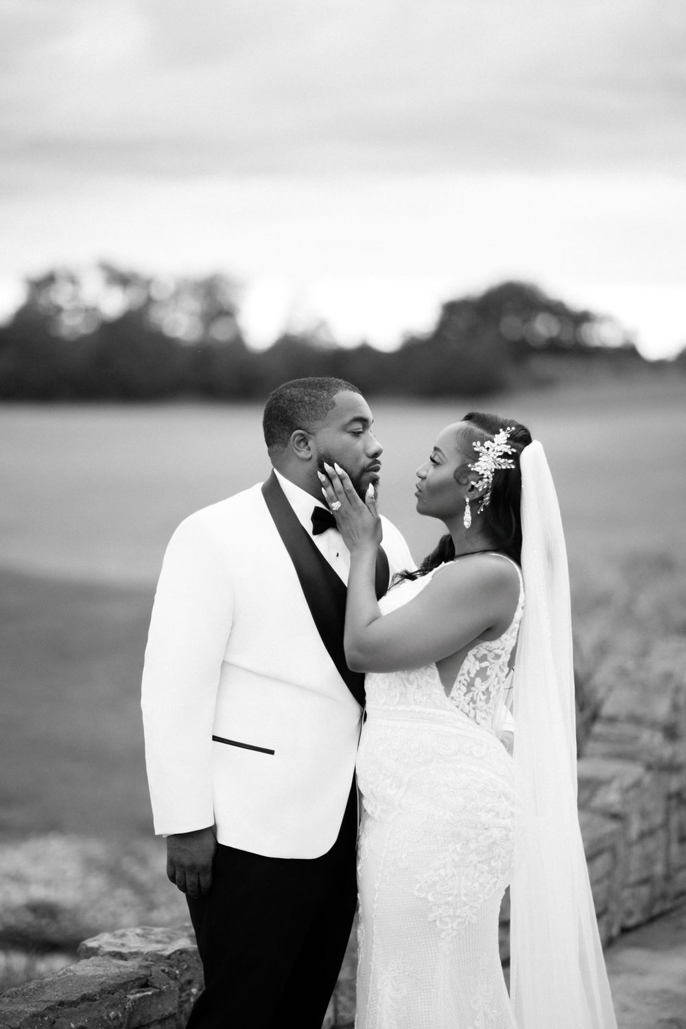 Joyful newlyweds share a candid moment together outdoors, with the bride in white lace and groom in white dinner jacket.