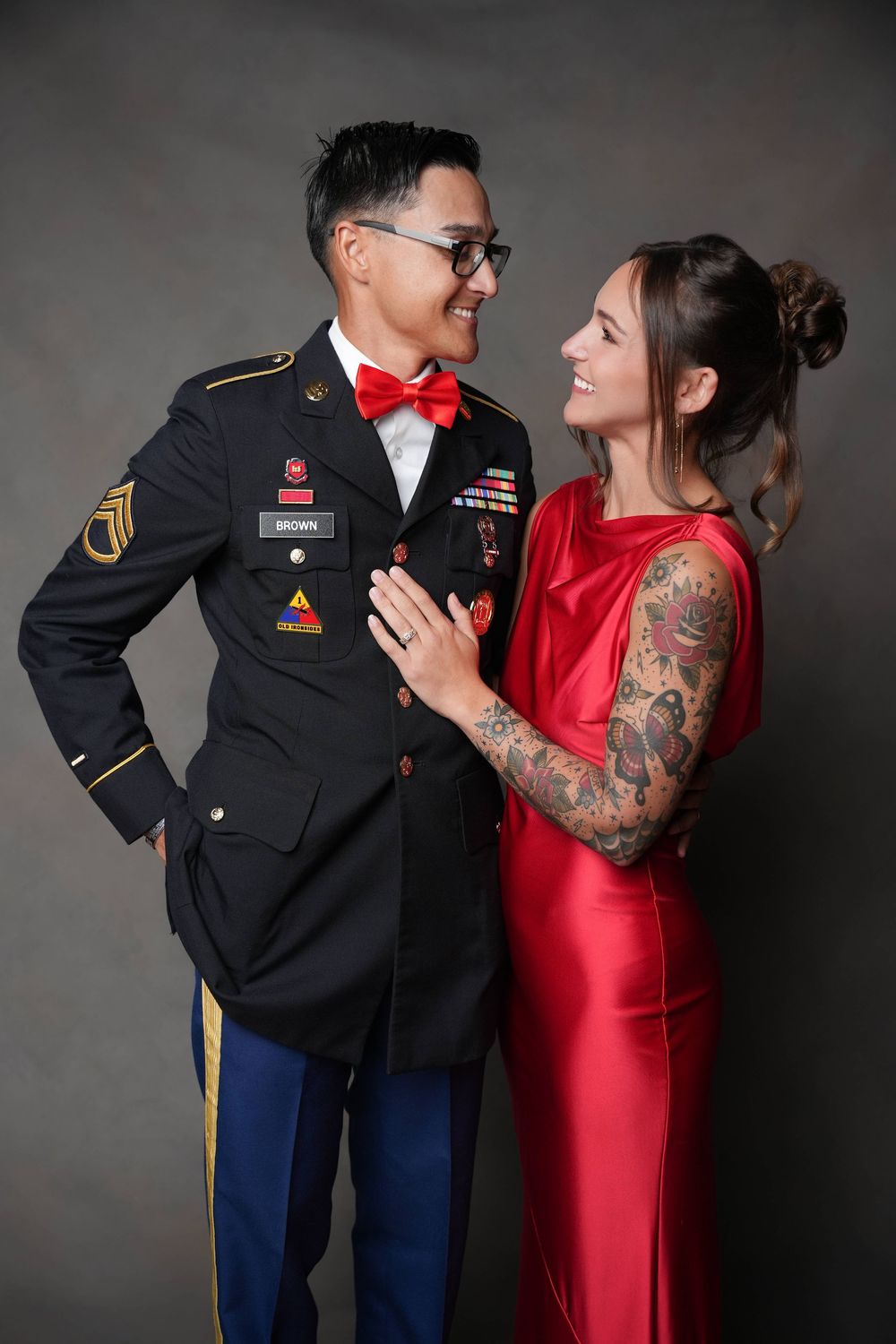 Couple in formal attire. Man in Army Dress Uniform and woman in Engineer Red formal dress hugging and posing in front of a  brown backdrop