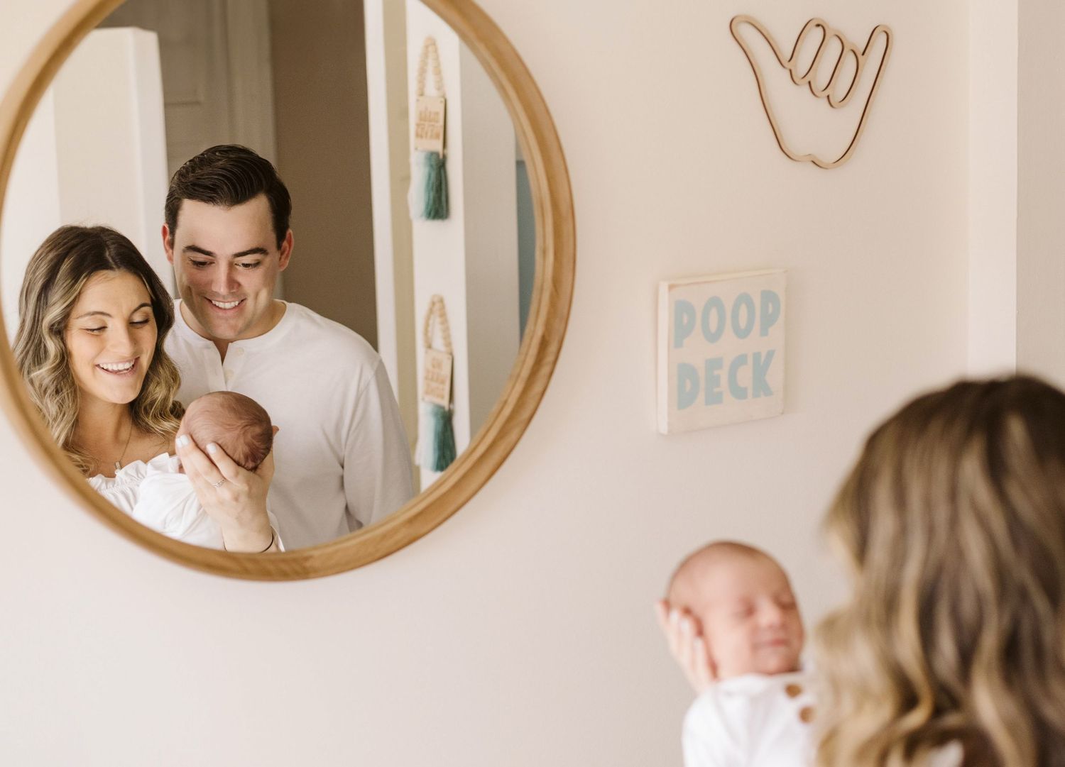 A family moment reflected in a round mirror with nursery wall decor visible.