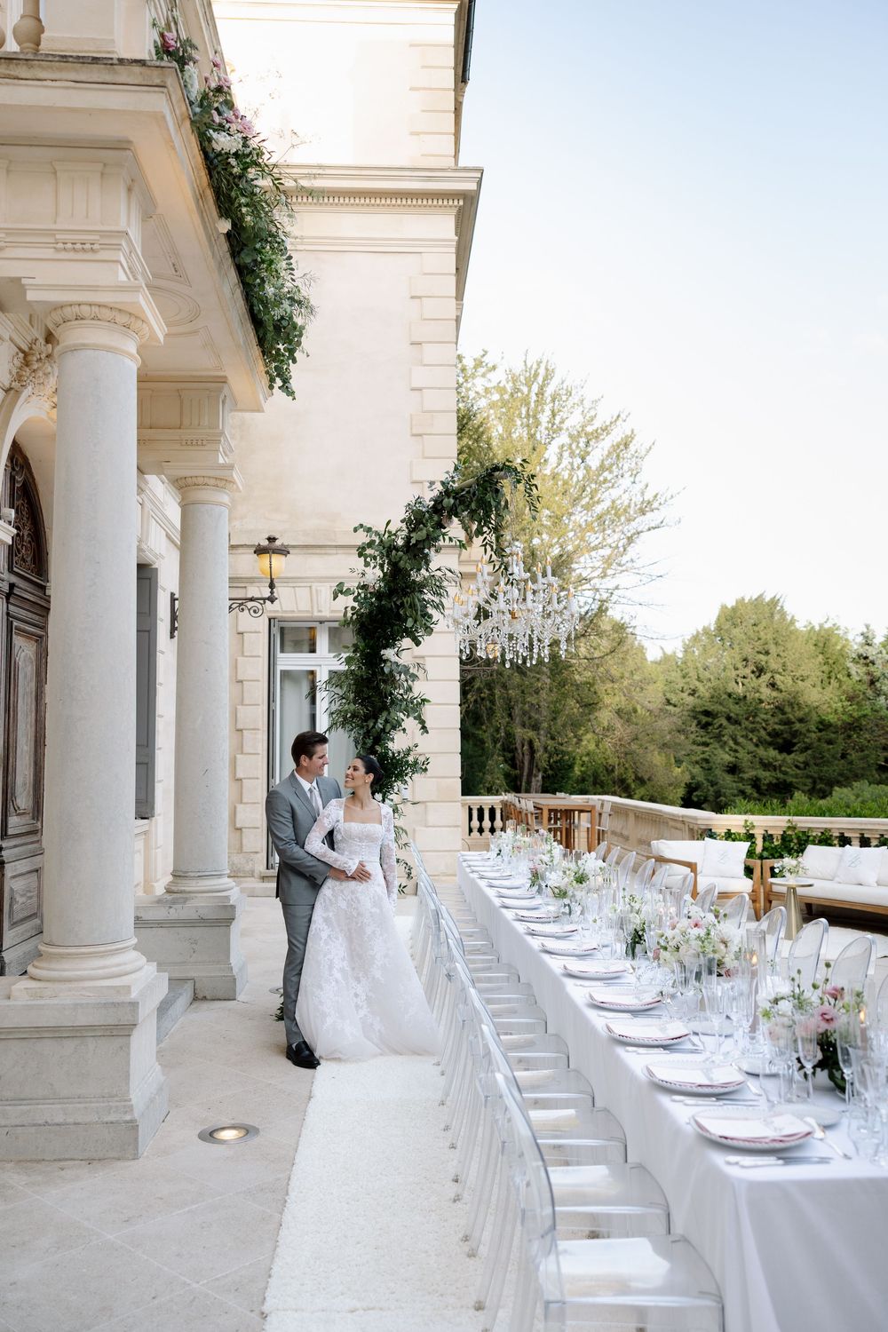 Elegant outdoor wedding reception setup with white tables and floral arrangements under columned portico.