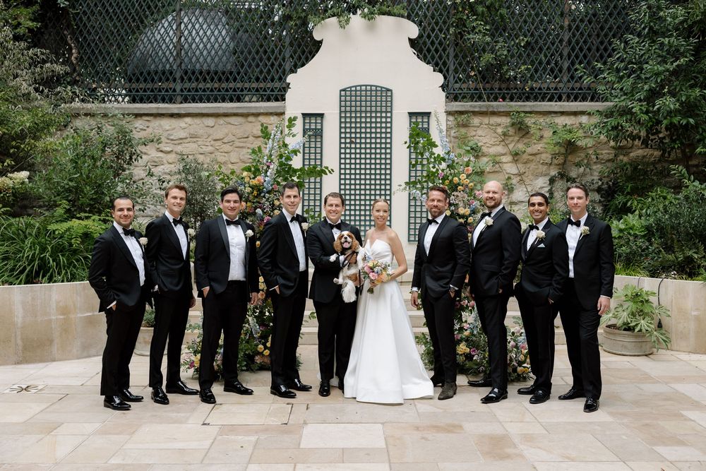 Wedding party in formal attire poses together on stone terrace.