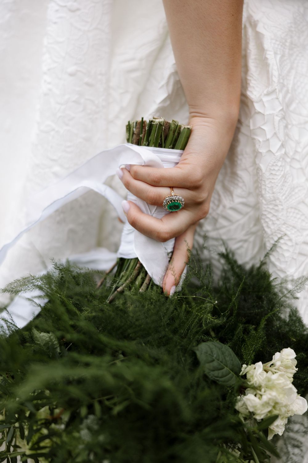 Close-up of hand holding wedding bouquet with emerald ring detail.