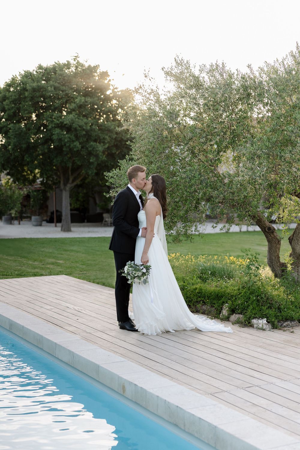 Romantic poolside wedding portrait at sunset with lush garden backdrop.
