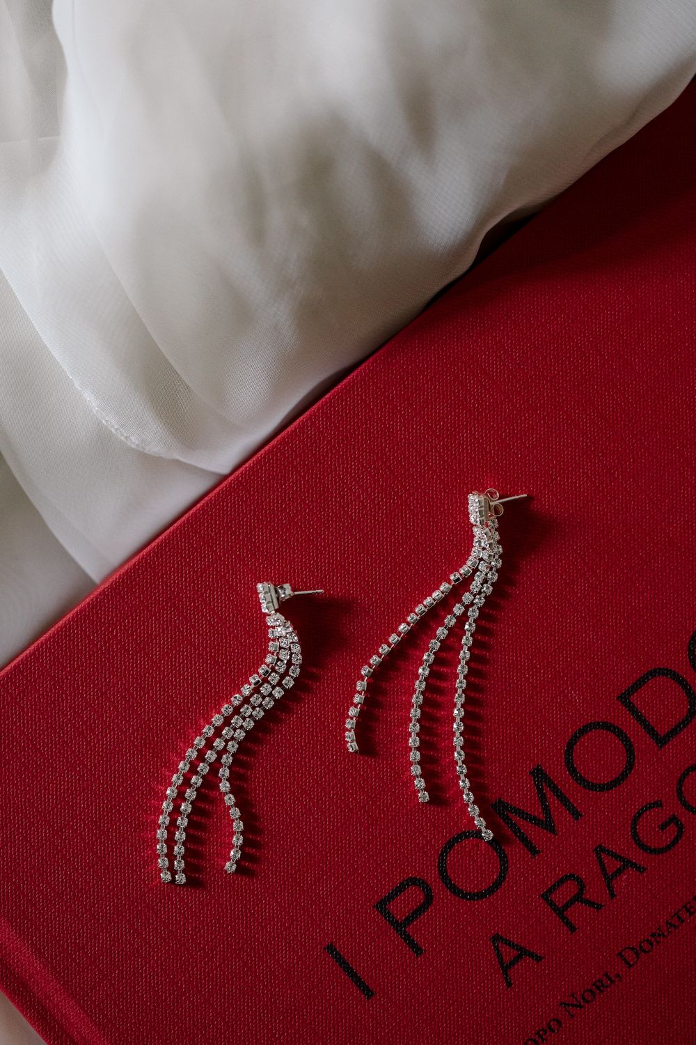 Crystal drop earrings displayed on red fabric with elegant branding.
