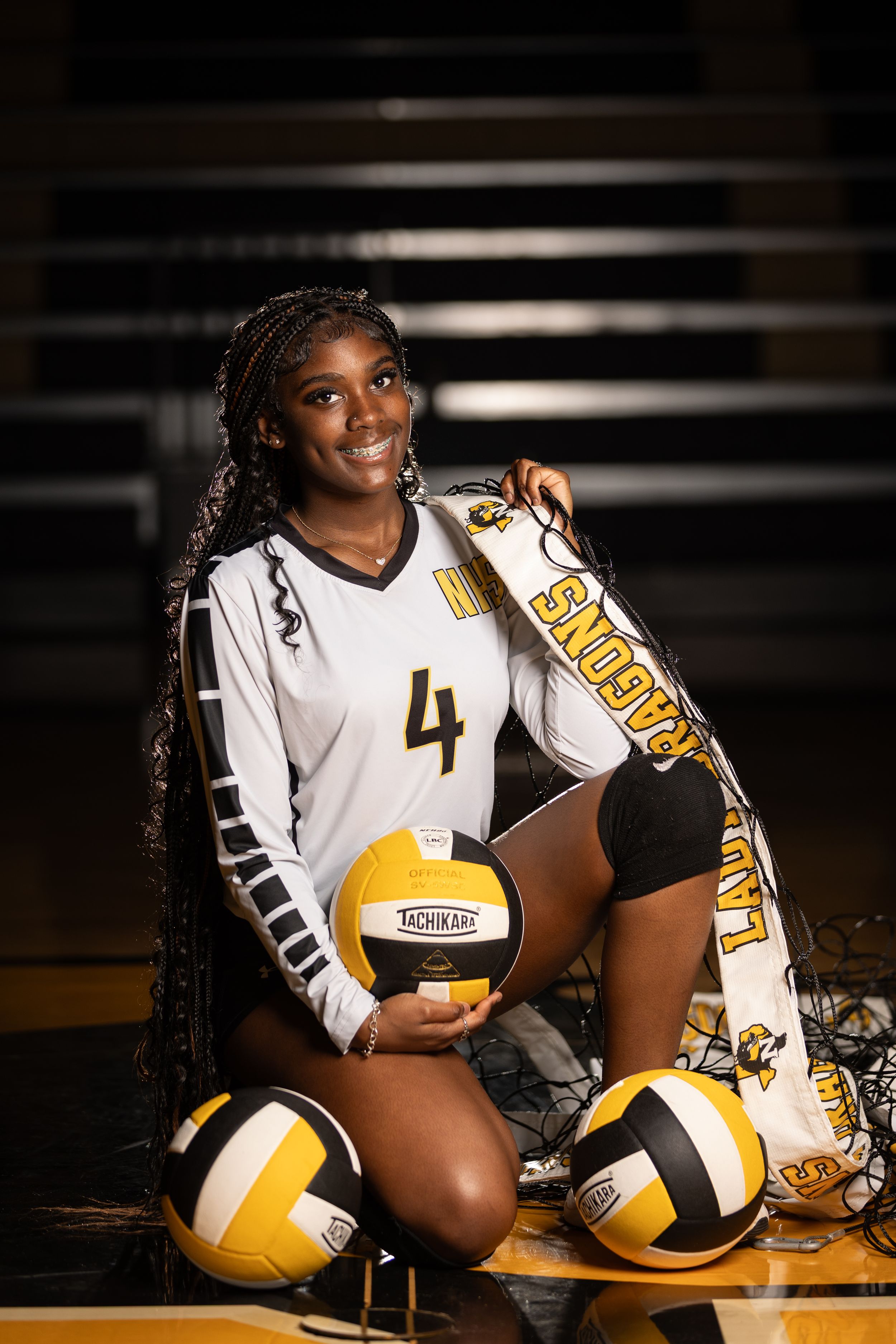 High school volleyball player poses with multiple volleyballs while wearing white and gold team uniform number 4.