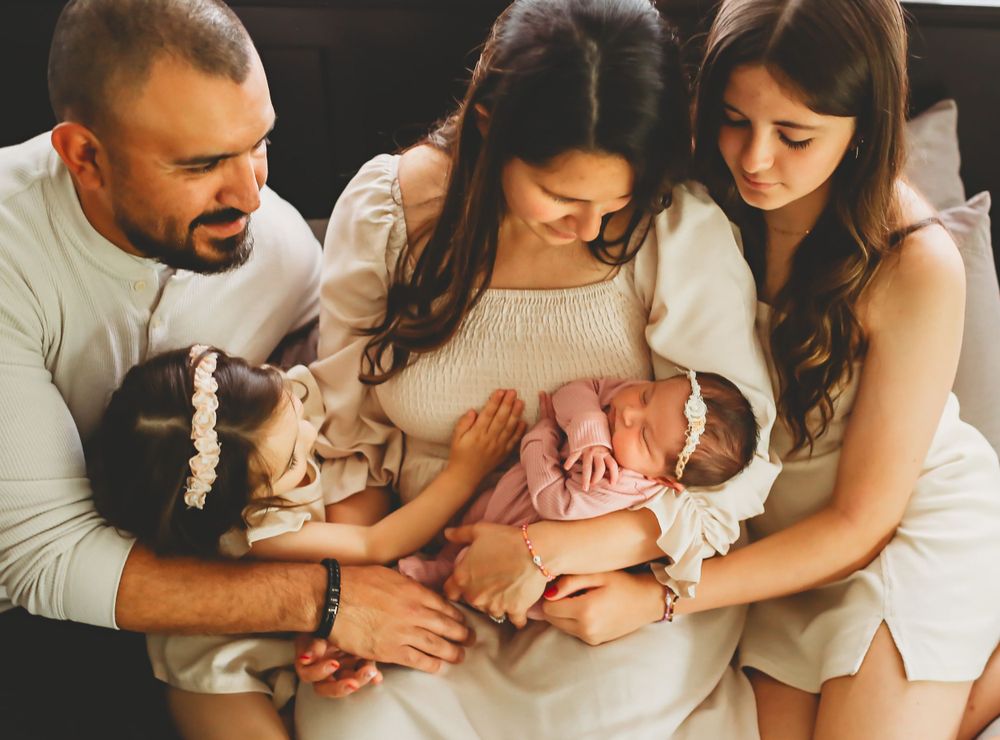Family sits together on couch tenderly holding newborn baby in pink outfit while showing affection and bonding.