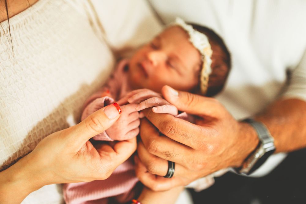 Close-up shot of hands trimming tiny fingernails on newborn baby wearing a white headband.