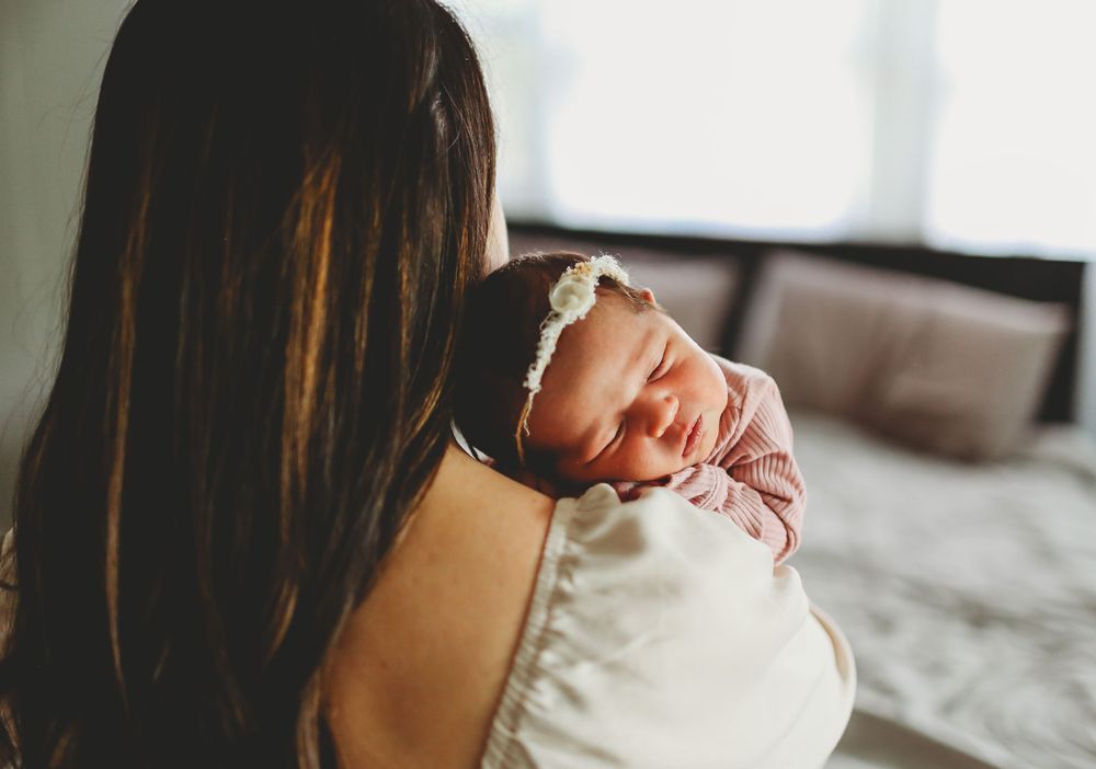 A peaceful newborn baby sleeps soundly on moms shoulder in a softly lit room.