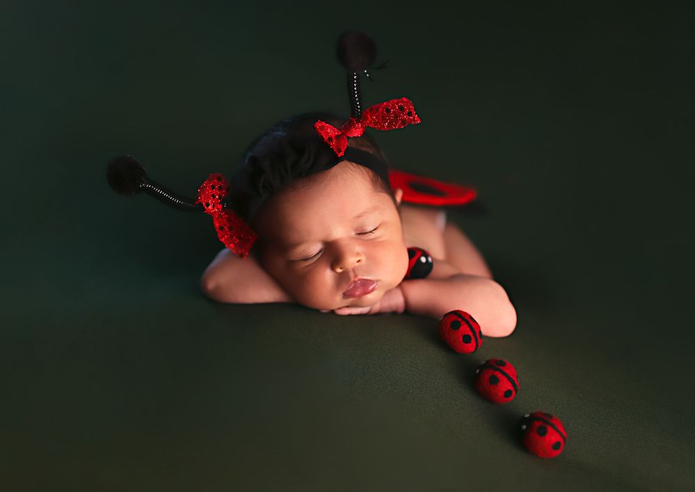 Sleeping newborn baby in red ladybug accessories with polka dots on green background during professional photoshoot.