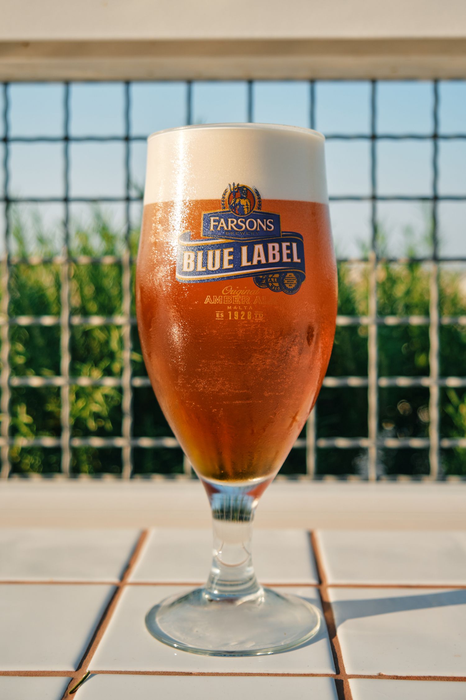 A glass of Parsons Blue Label beer with a frothy head against a window background.