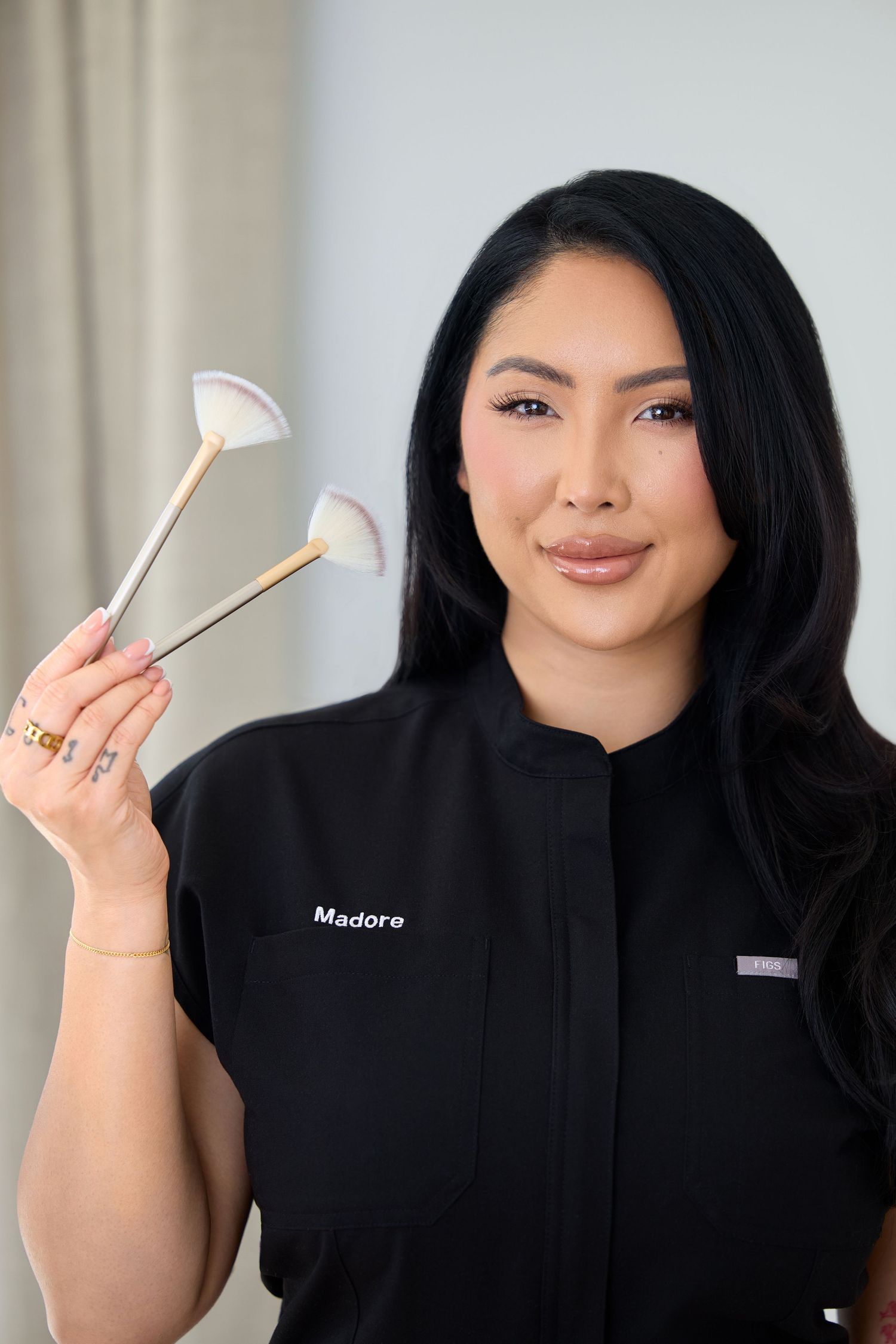 Professional wearing black uniform holds facial massage tools against light background showing spa treatment tools.