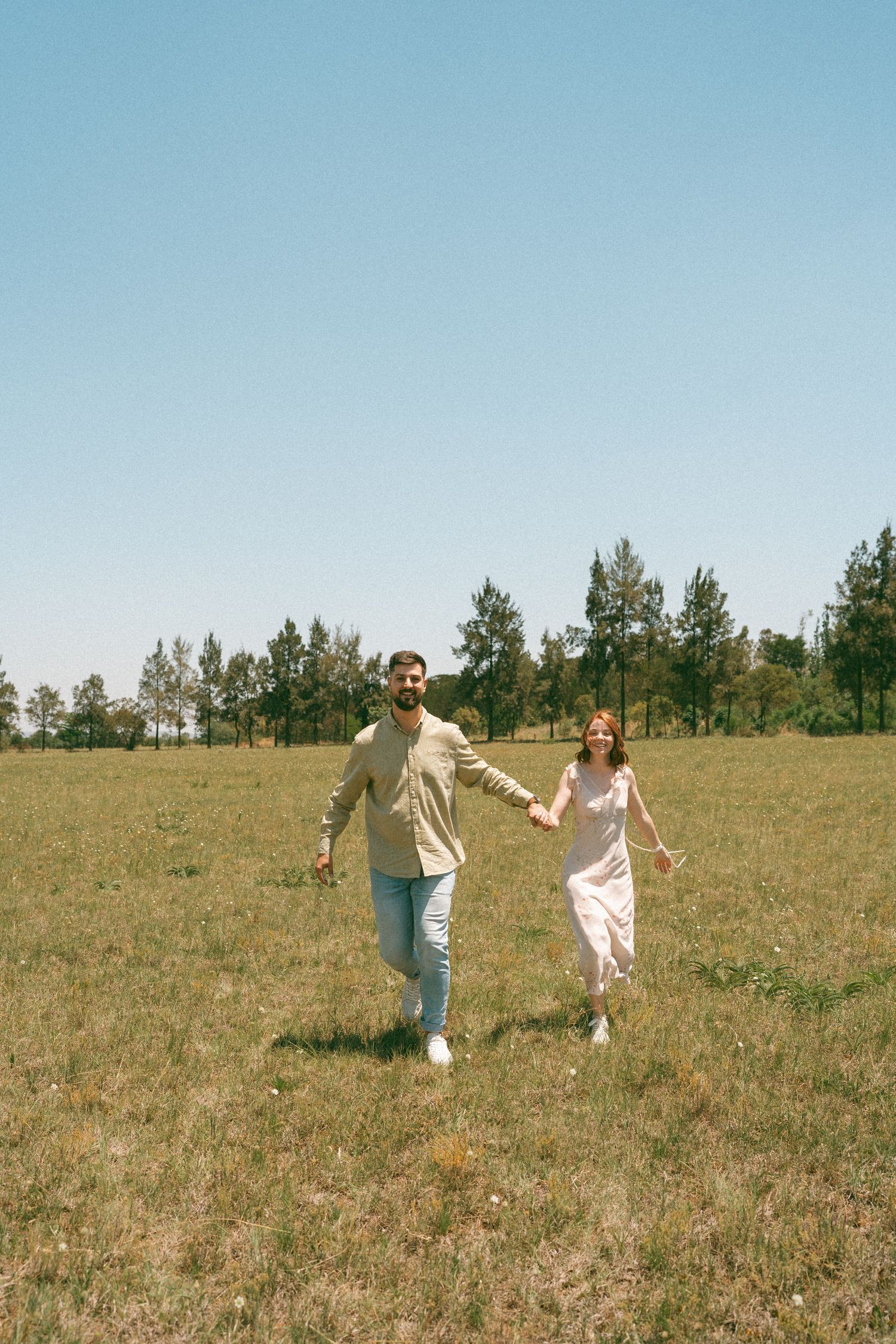 Playful dance sequence in a sunny field with trees and blue sky in the background.
