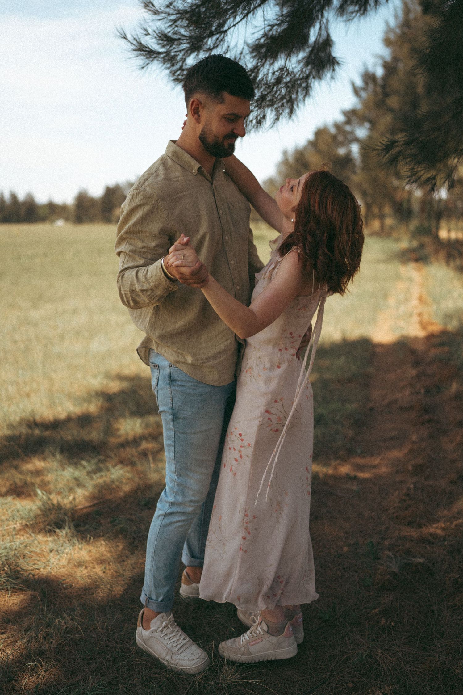 A couple in casual attire sharing a dance moment under pine trees.