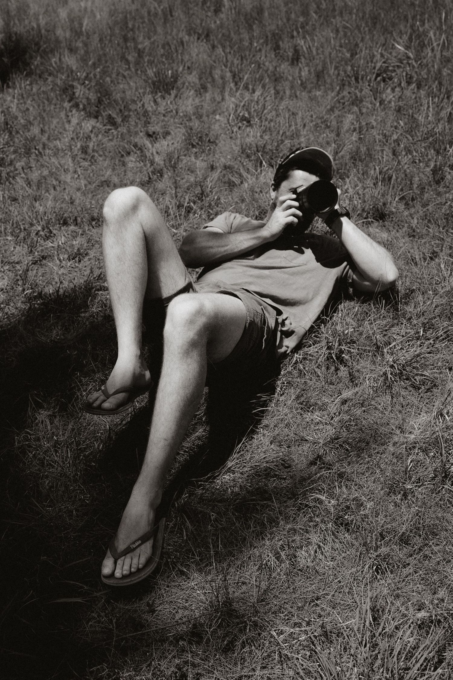 Black and white image of someone lying in tall grass, showing only their legs and feet.