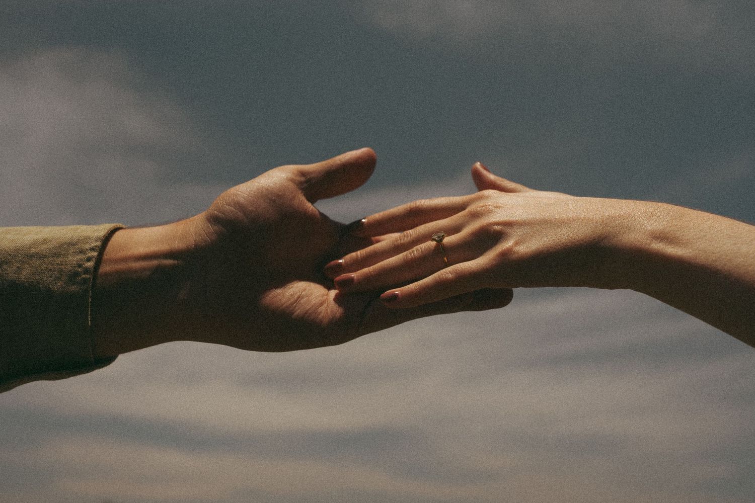 Multiple hands reaching out towards each other in a dramatic sunset lighting.