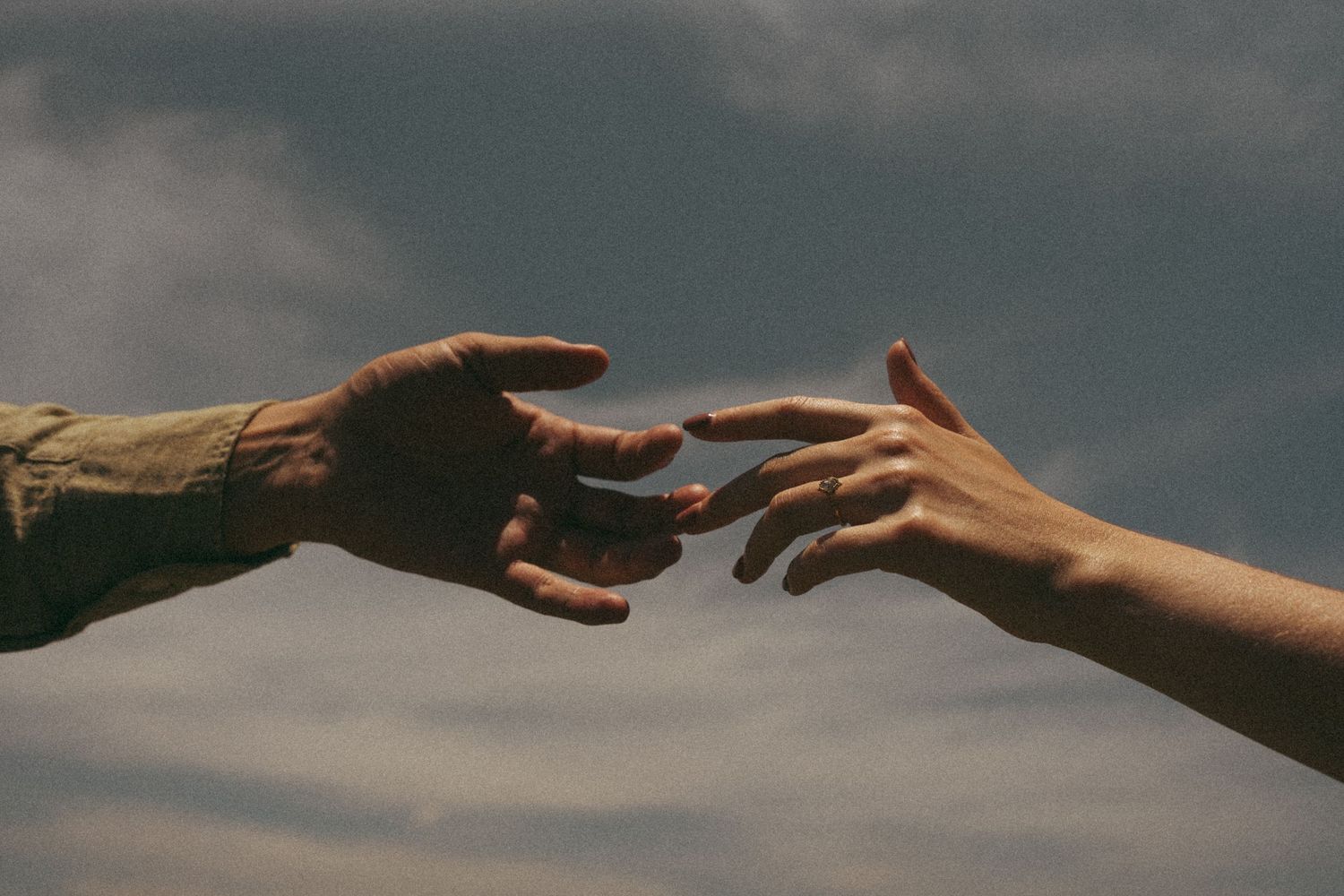 Two hands reaching towards each other against a cloudy sky background.