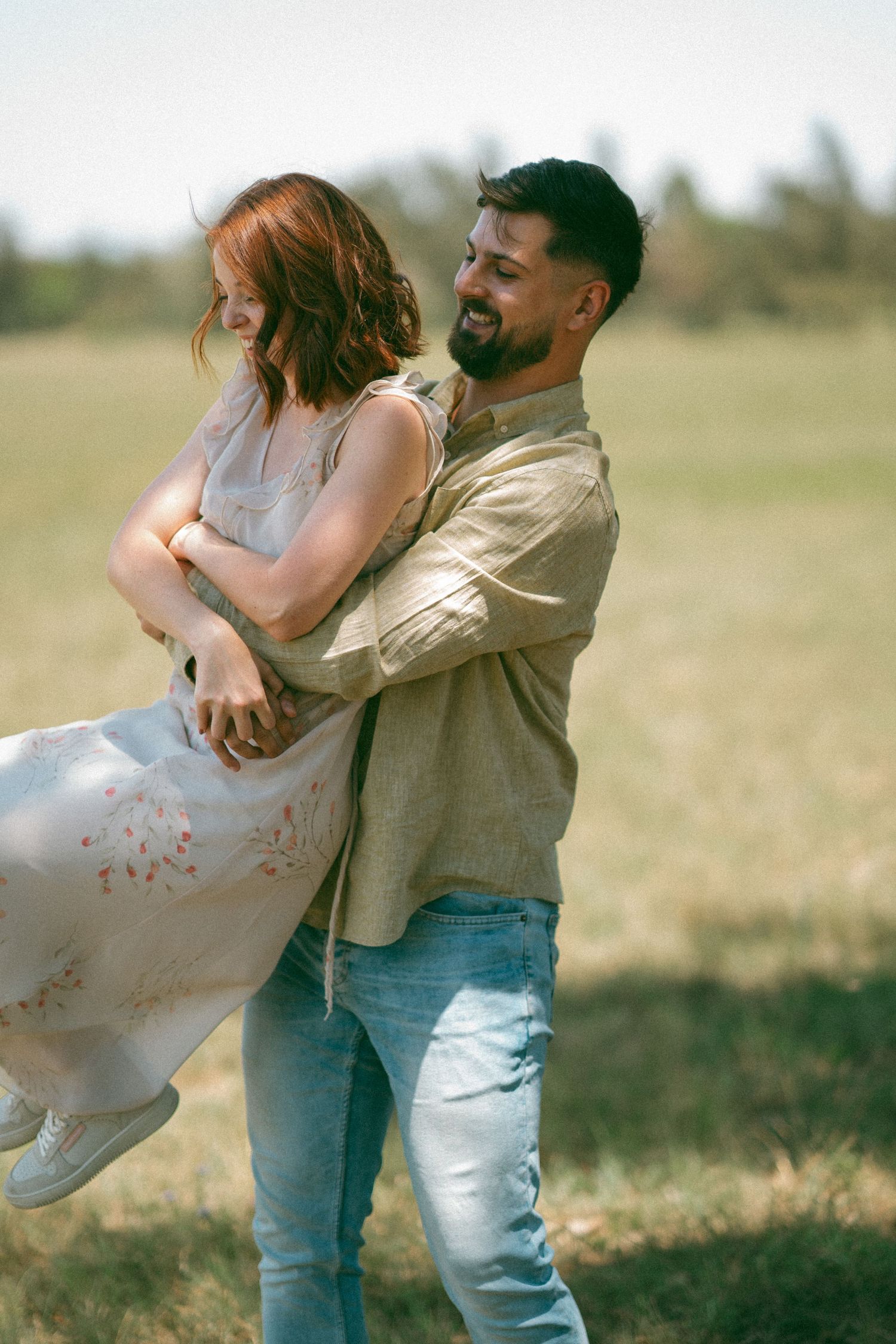 A couple shares a joyful embrace while spinning in a grassy field.