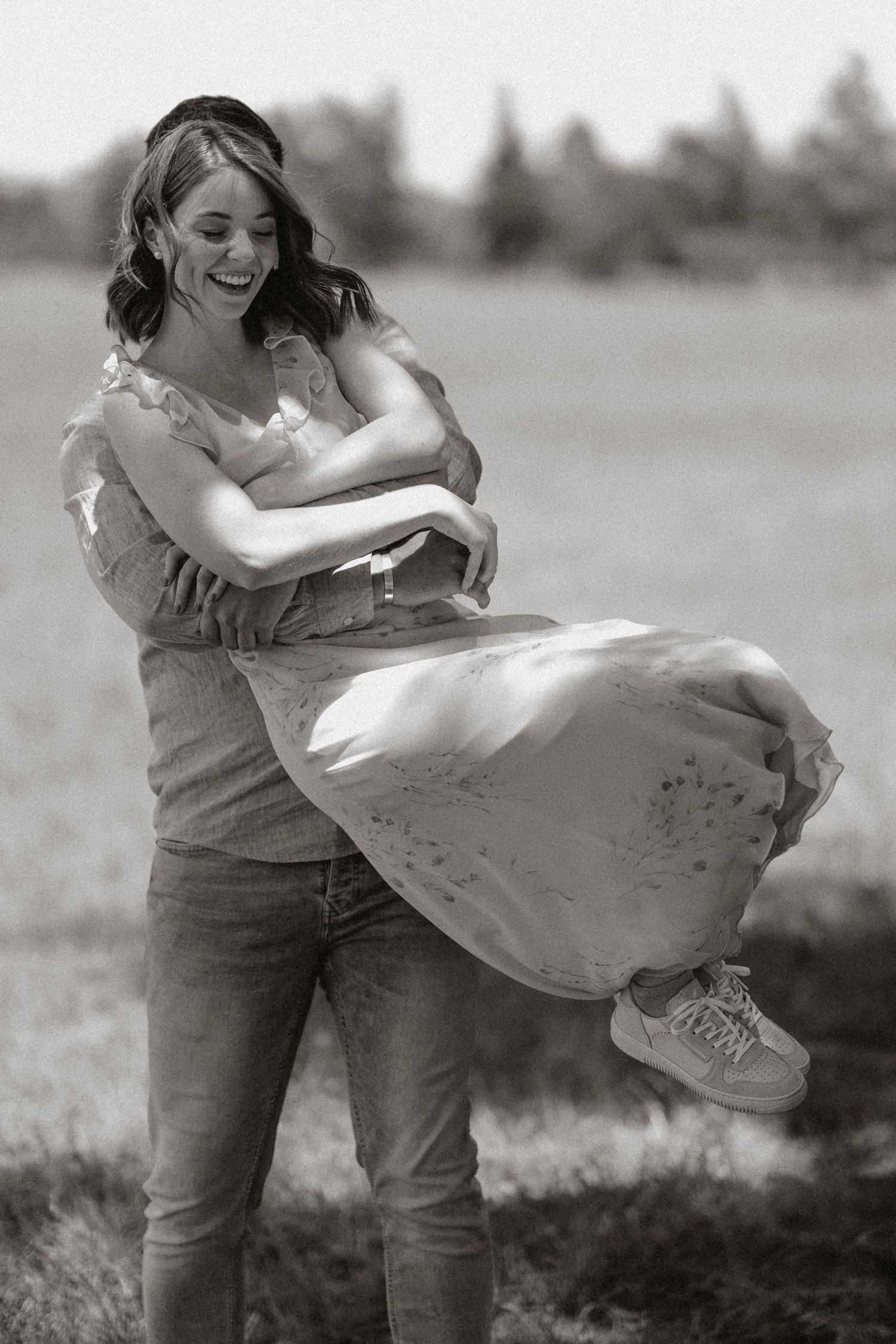 Black and white photo of a couple dancing and laughing together in nature.