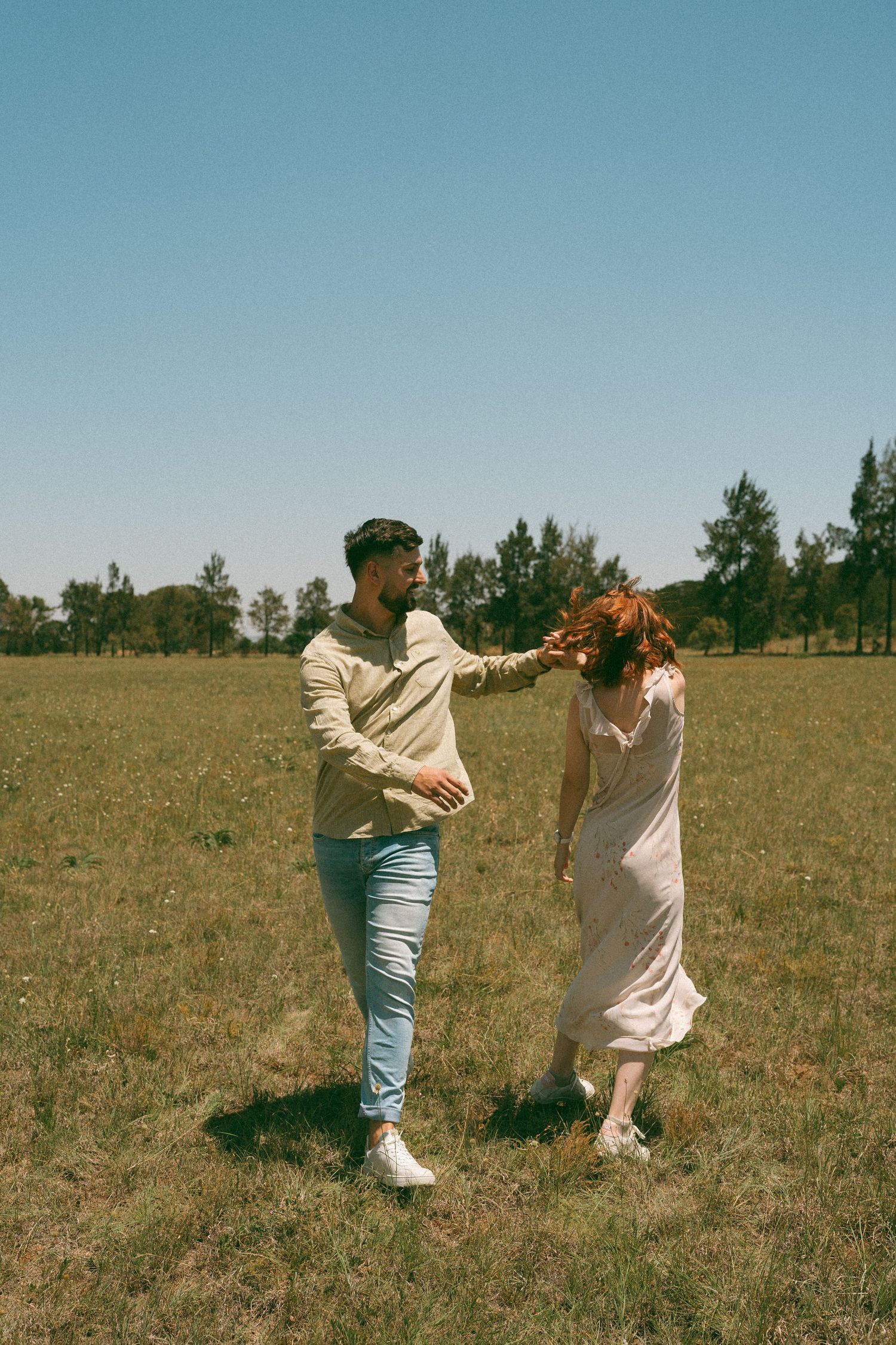 Two people dance and spin together in a sunny meadow on a clear day.