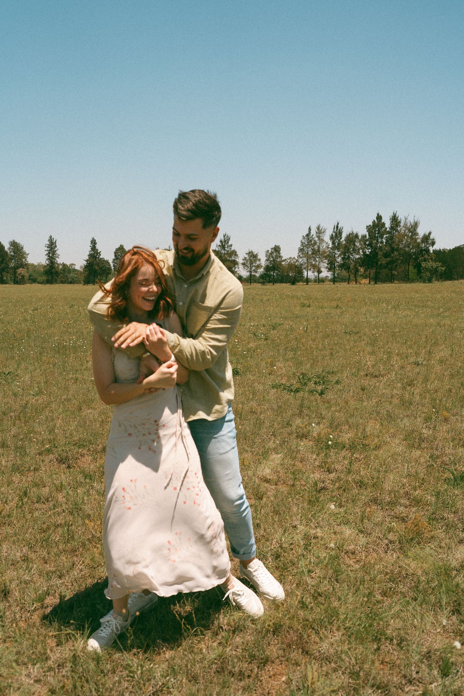 A couple shares a romantic dance move in an open field under blue skies.