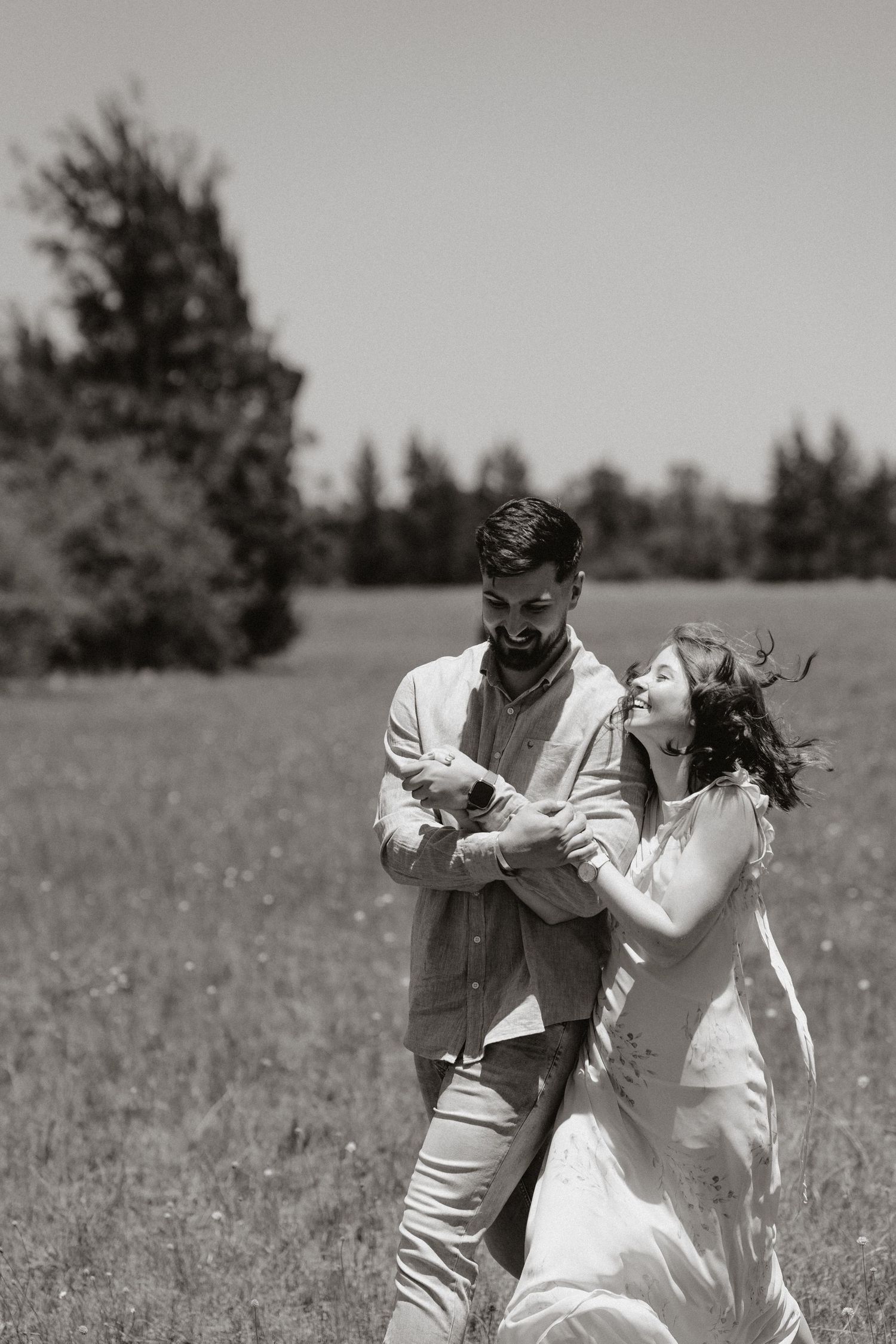 Black and white photo of couple dancing playfully in open field.