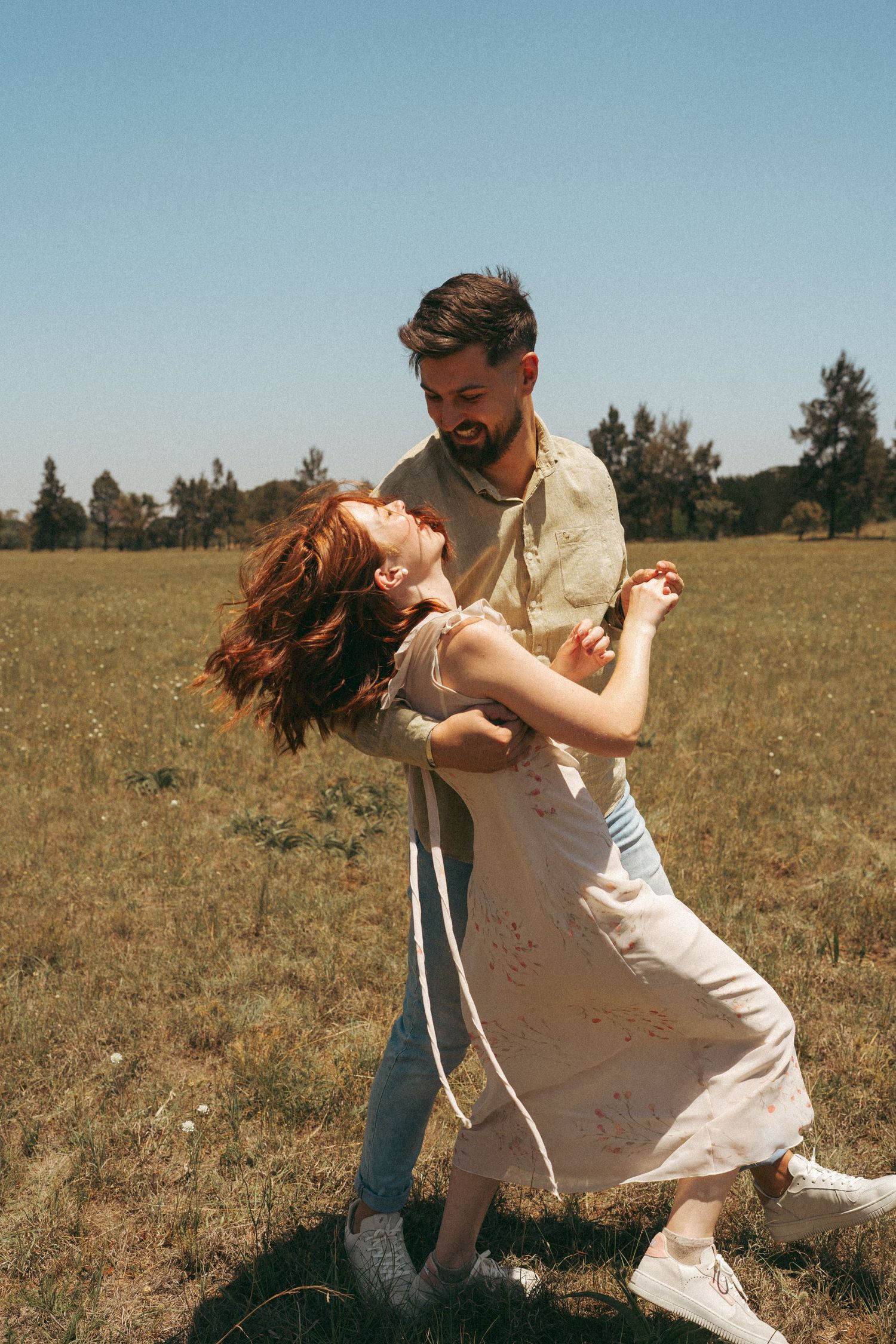 A couple spins and dances together in a sun-lit meadow.
