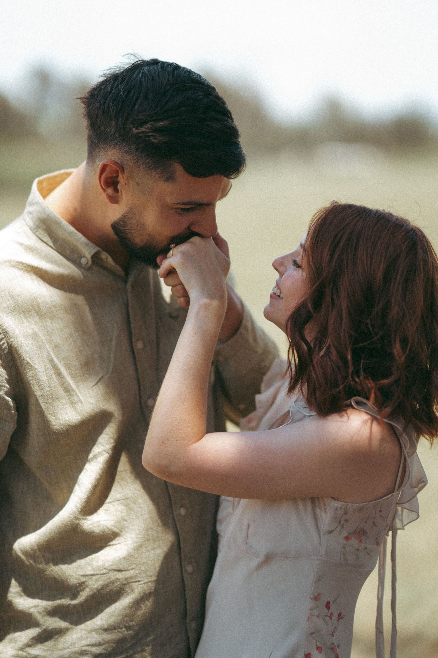 A romantic couple shares an intimate moment in a field, with the woman tenderly touching the man's face.