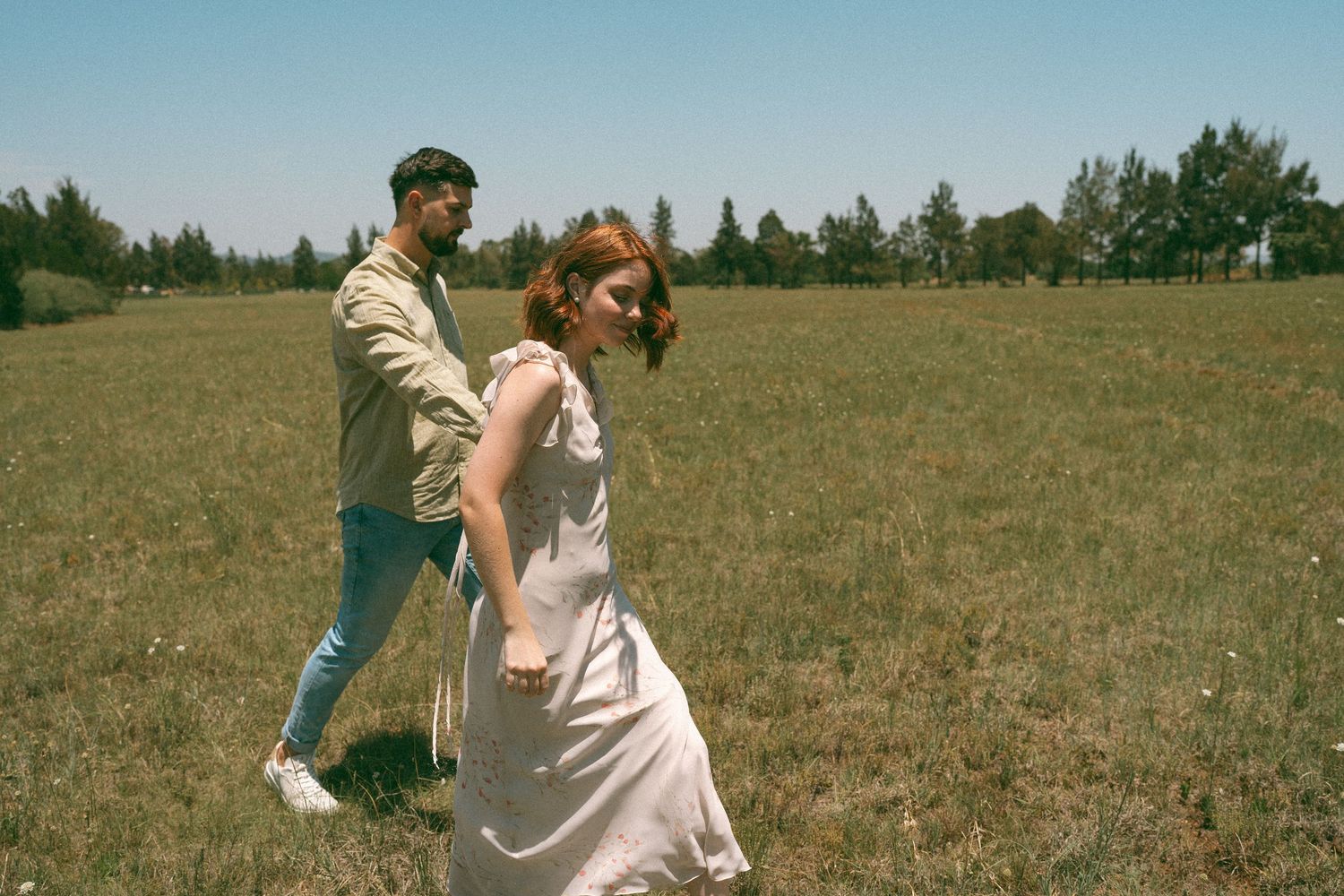 A playful couple dances together in an open field on a bright summer day.