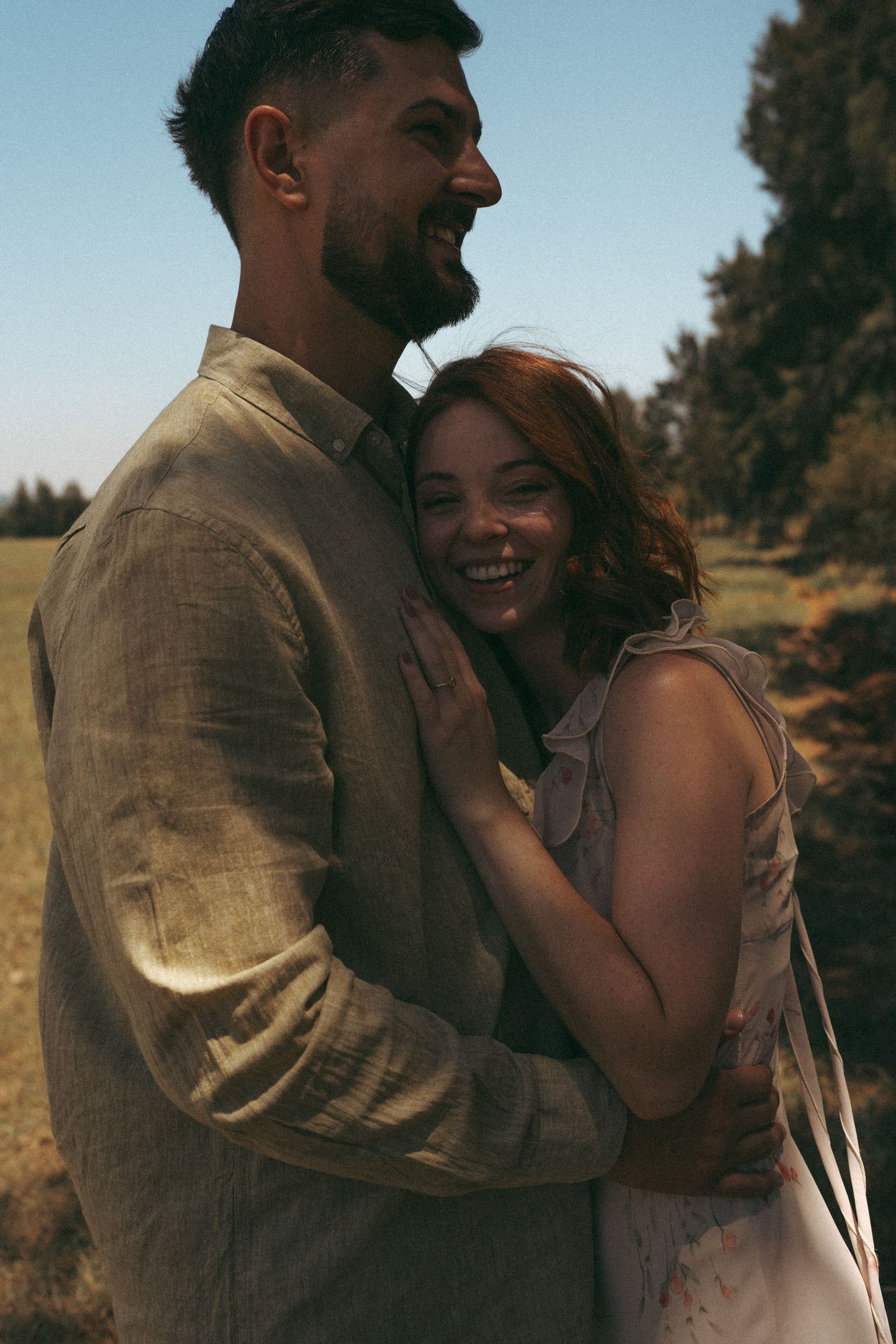 A couple embraces and laughs together in a sun-drenched field during golden hour.