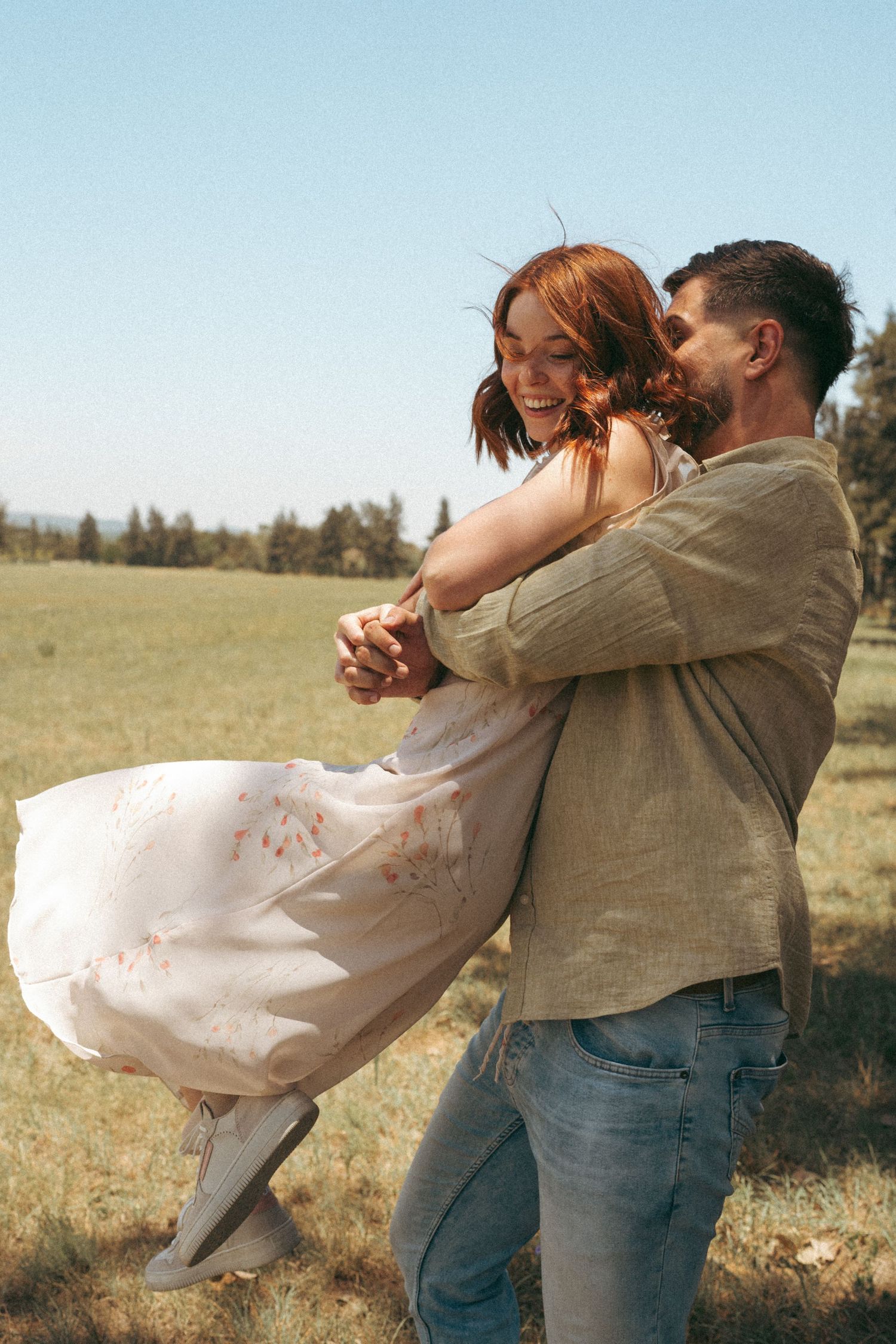 Playful couple in light colored clothing dancing in an open field.