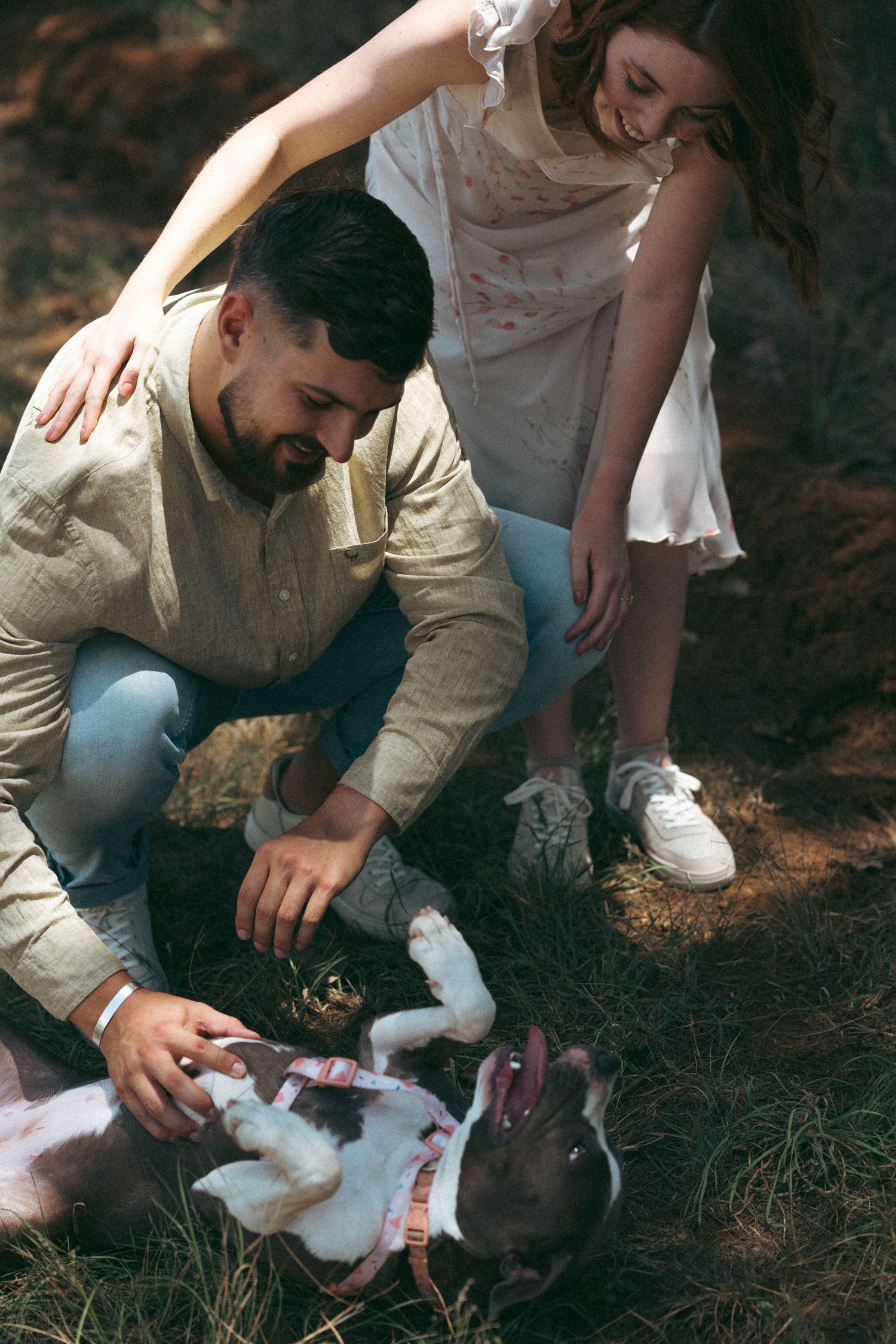 A couple plays with their black and white dog on the ground outdoors.