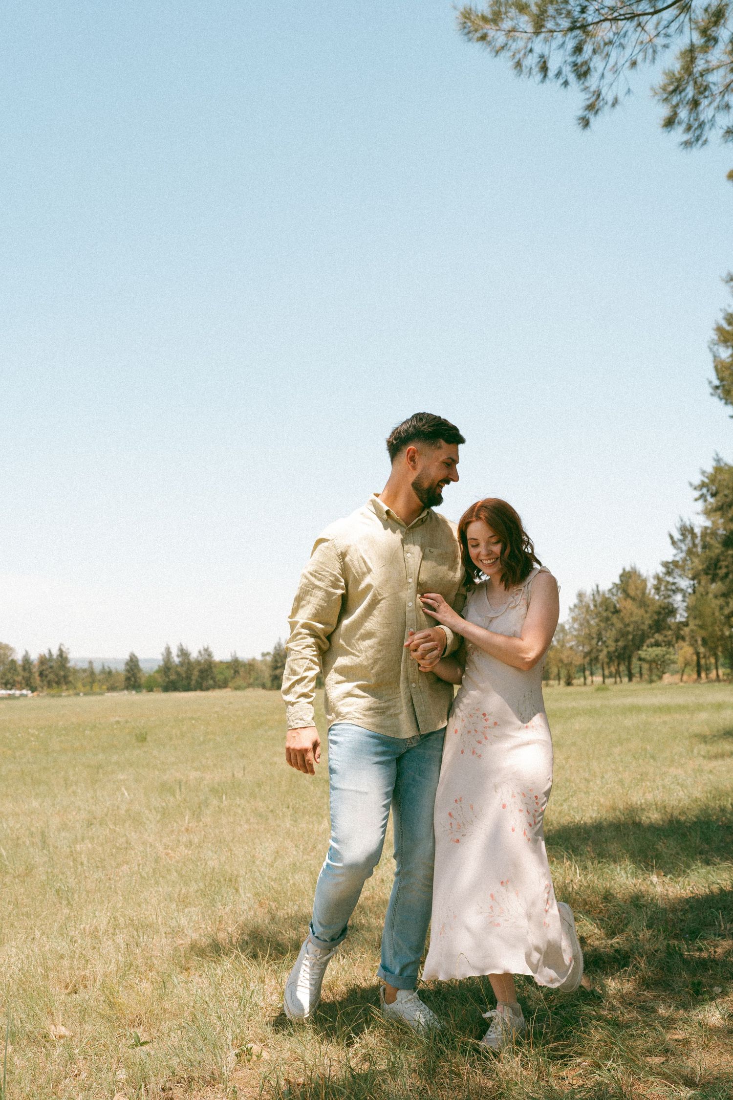 Couple dancing together in a sunny meadow with pine trees in the background.
